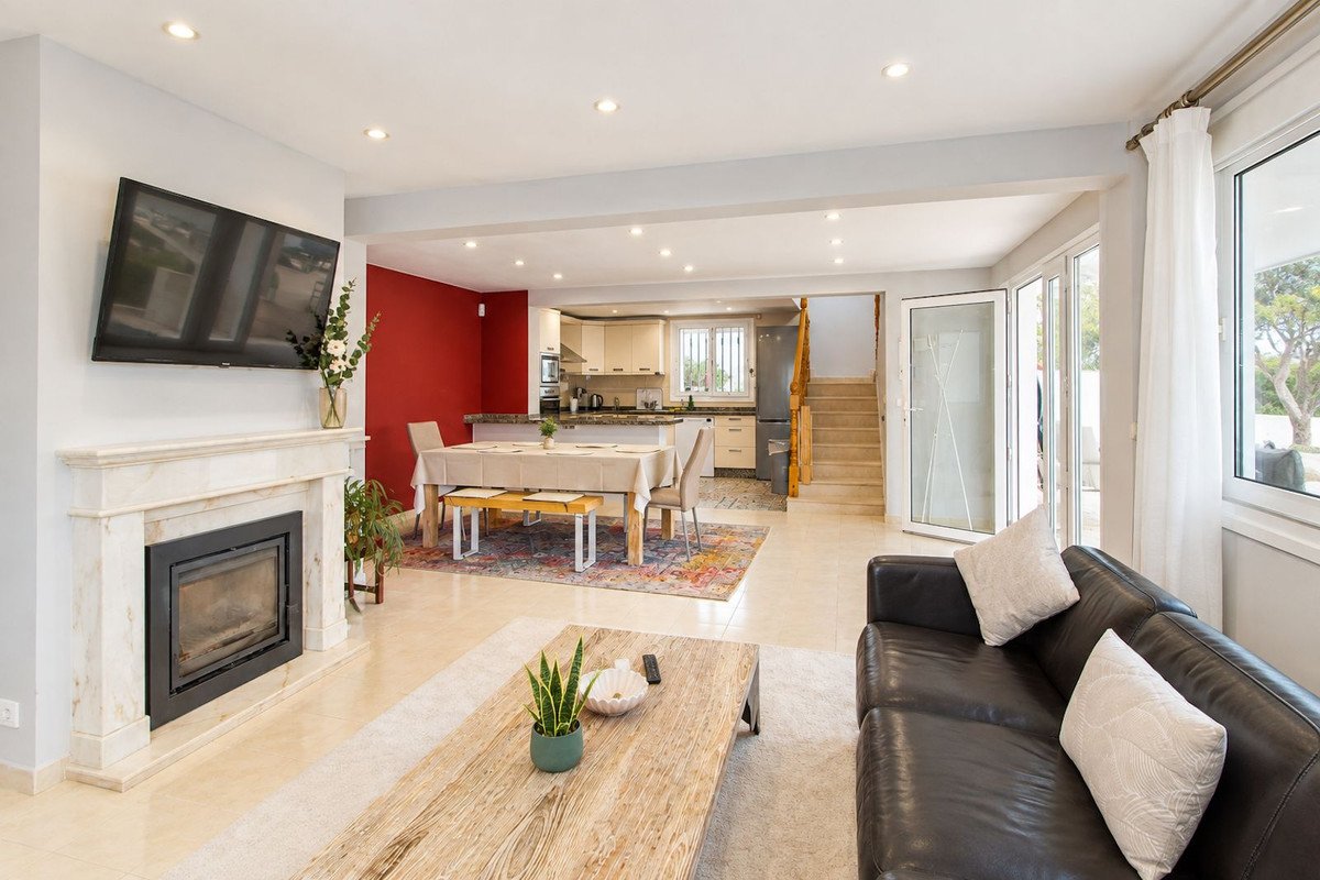 Open-plan living area with fireplace, dining table, and modern kitchen. Large windows offer natural light.