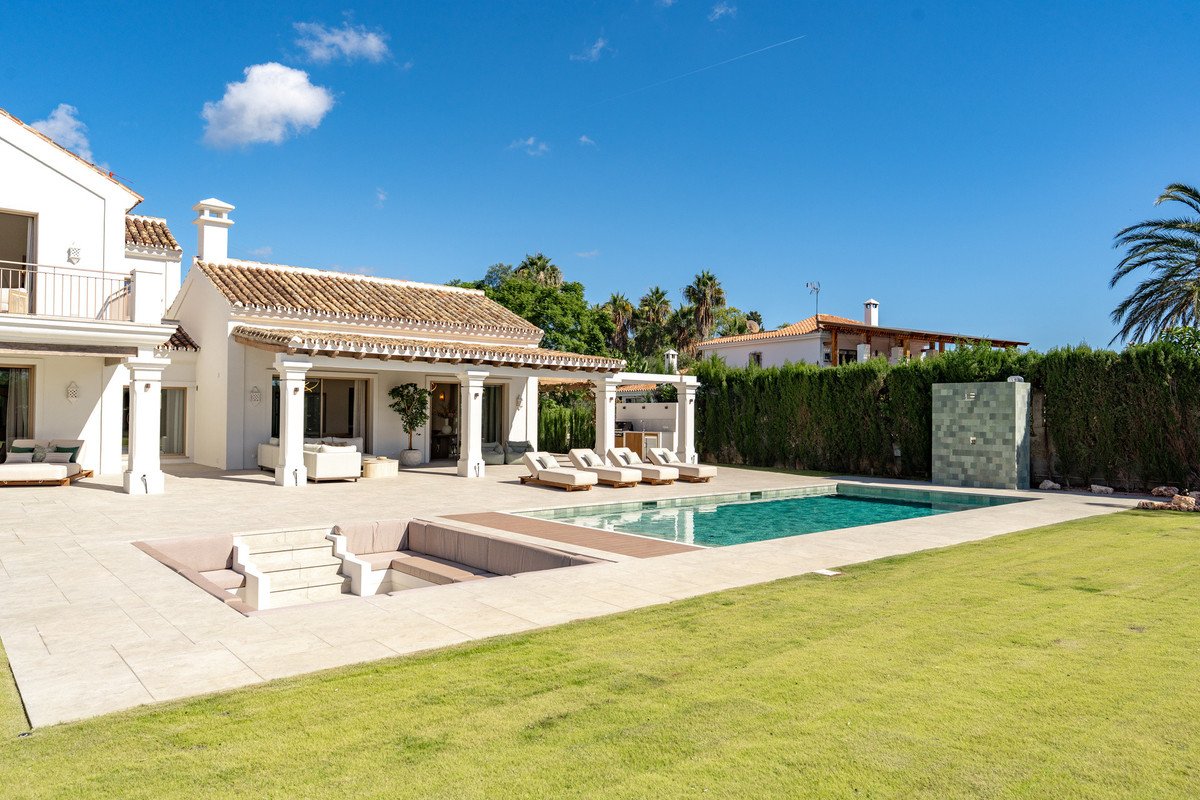 Luxury villa with swimming pool, outdoor seating, and manicured lawn under clear blue sky