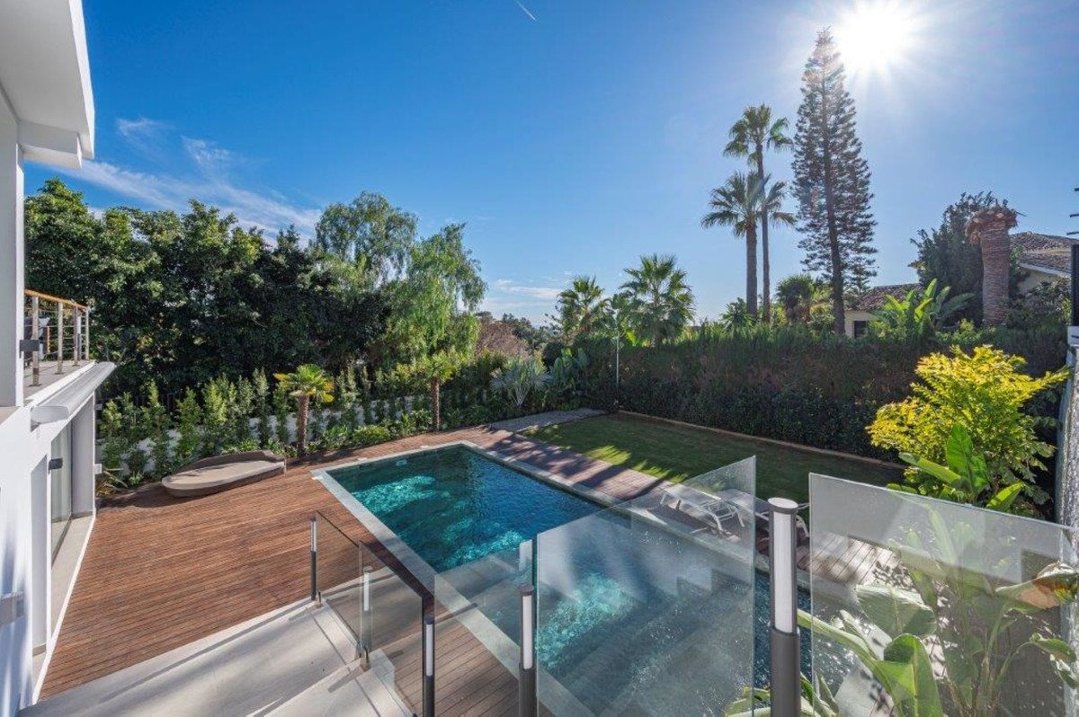View of a modern swimming pool, wooden deck, and lush green lawn under a bright sunny sky.