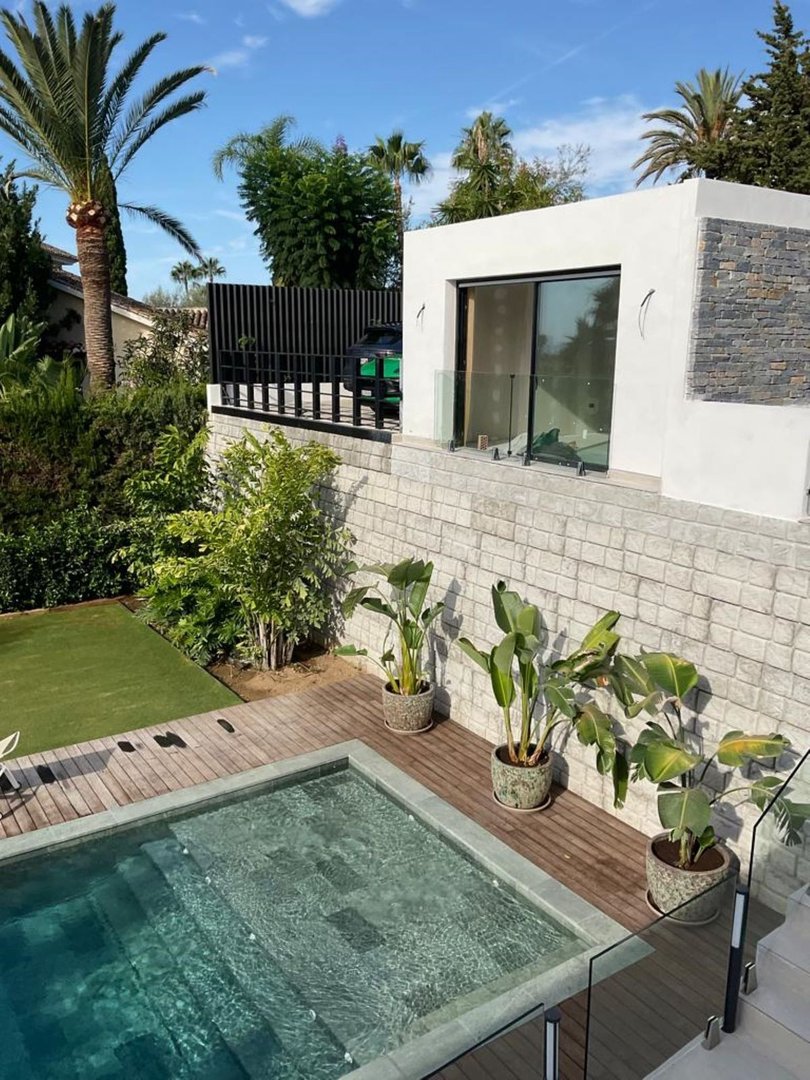 Luxury modern villa with a swimming pool, wooden deck, tropical plants, and lush green garden.