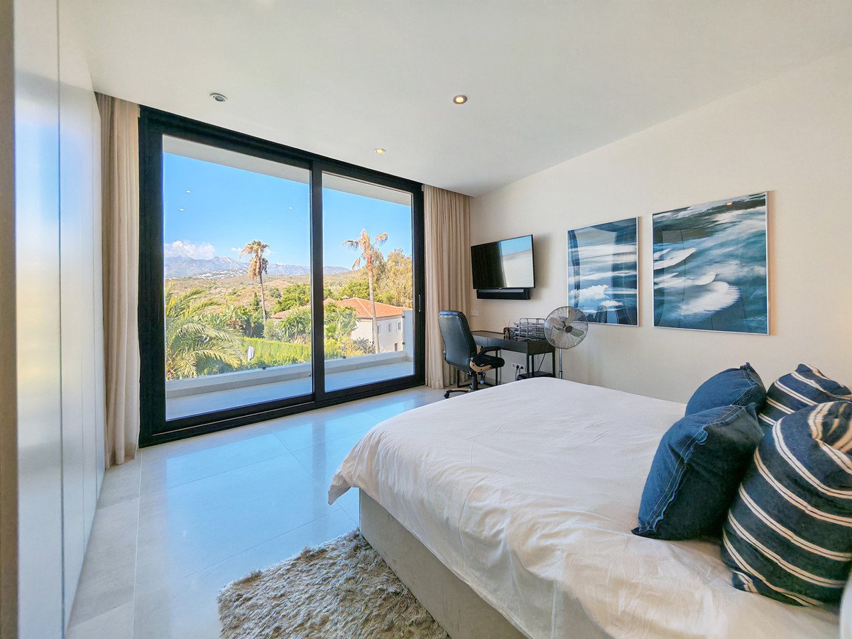Modern bedroom with large sliding glass doors, mountain and palm tree view, white bed, and blue accent pillows