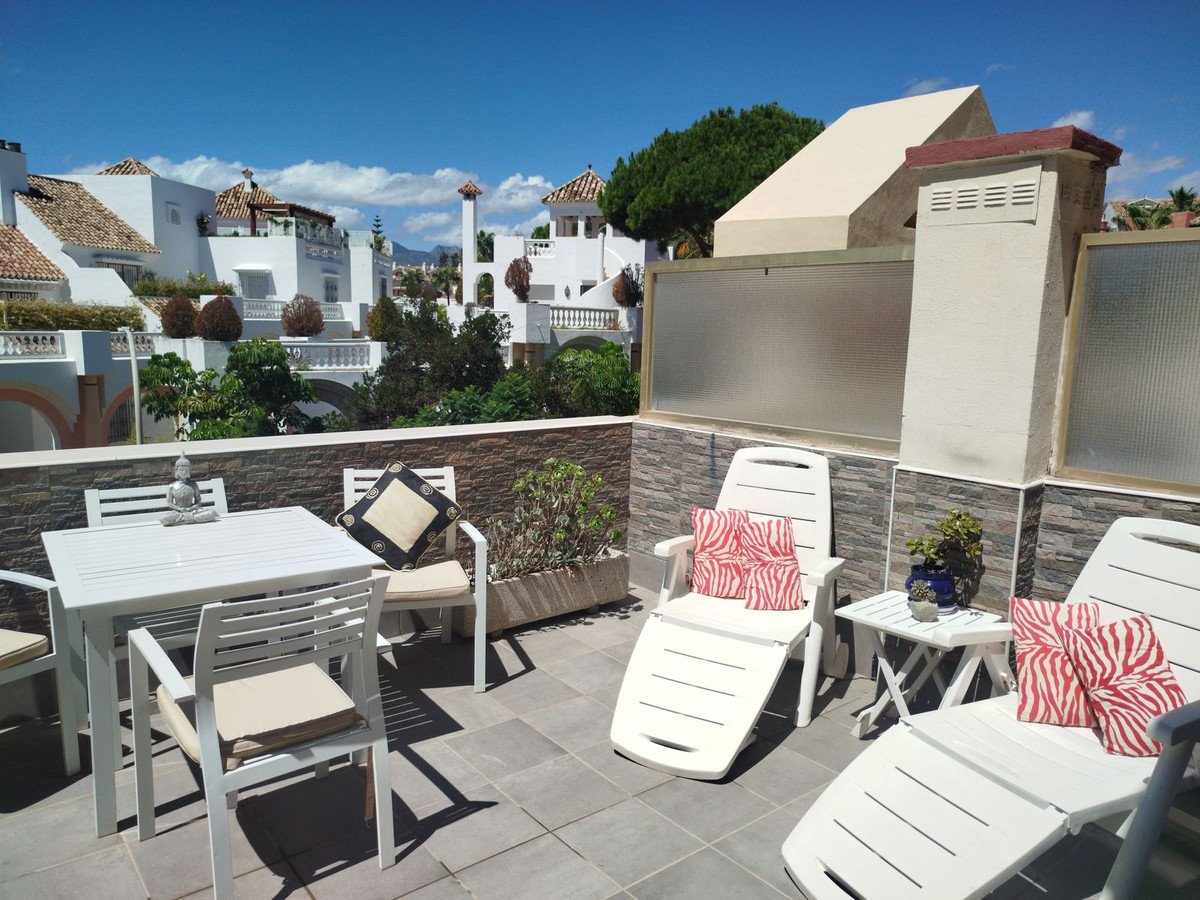 Terrace with dining set, sun loungers, and a beautiful view of white buildings and the sea under a clear blue sky.