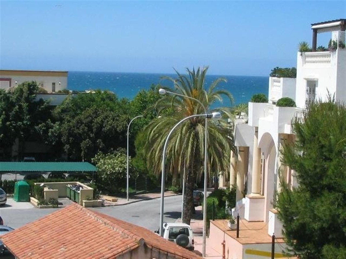 Balcony with sea view, featuring palm trees and Mediterranean architecture. Sunny day with blue sky.