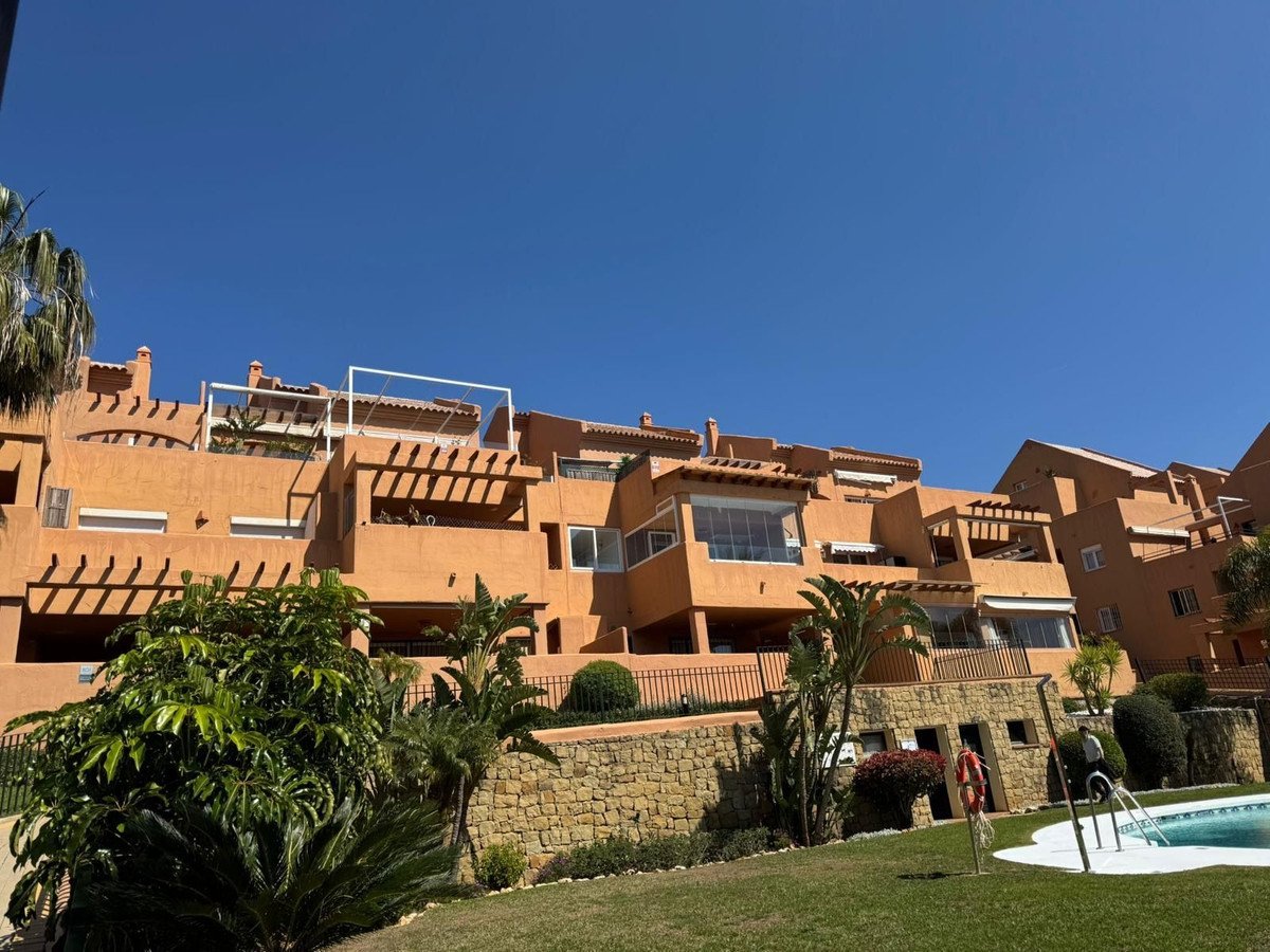 Orange apartment complex with terraces, pool, and tropical landscaping under blue sky