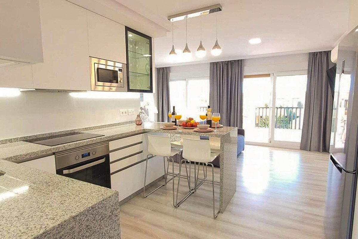Modern kitchen with island breakfast bar, built-in microwave, oven, and balcony view through sliding doors.