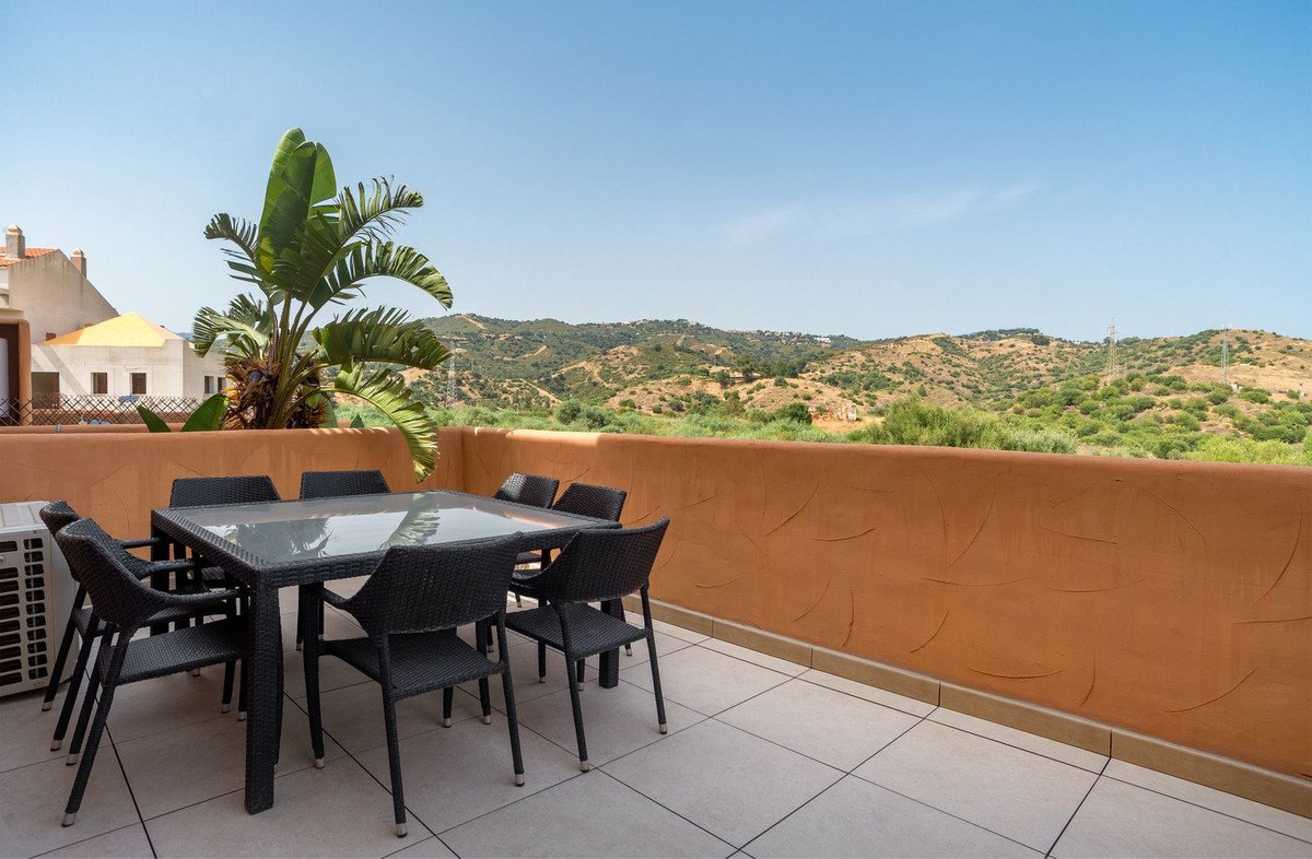 Terrace with dining table and chairs overlooking rolling hills and mountains under a clear blue sky.