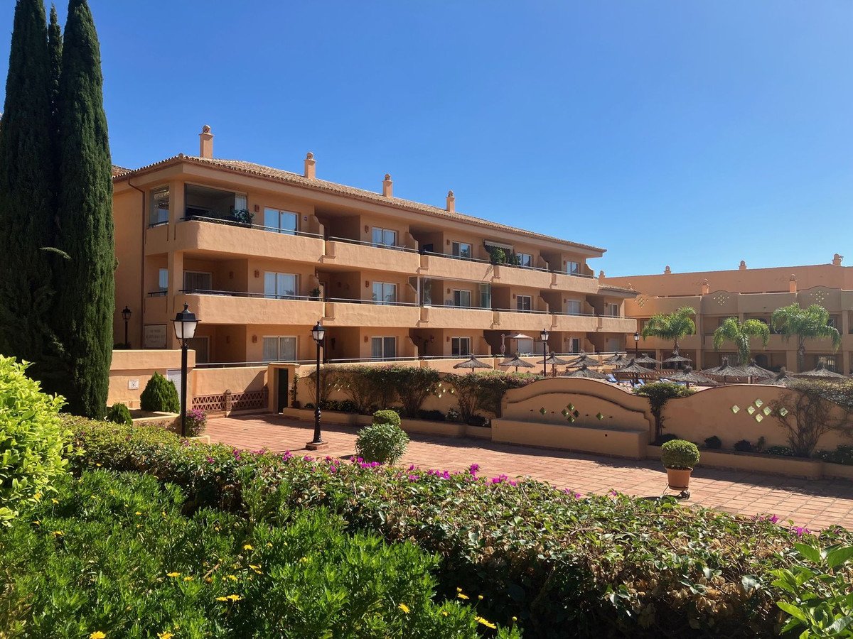 Apartment building exterior with balconies and a courtyard featuring a swimming pool and sun loungers under umbrellas.