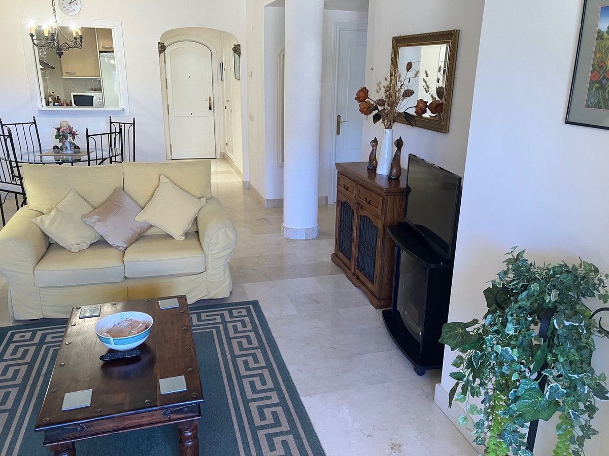 Living room with a beige sofa, coffee table, TV, wooden cabinet, and a reflection of the dining area and kitchen in a mirror.