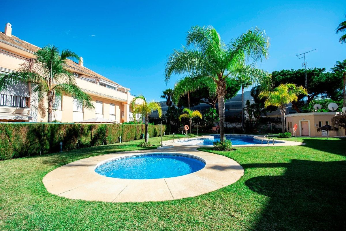 Apartment complex with swimming pools, palm trees, and well-maintained garden under clear blue sky.