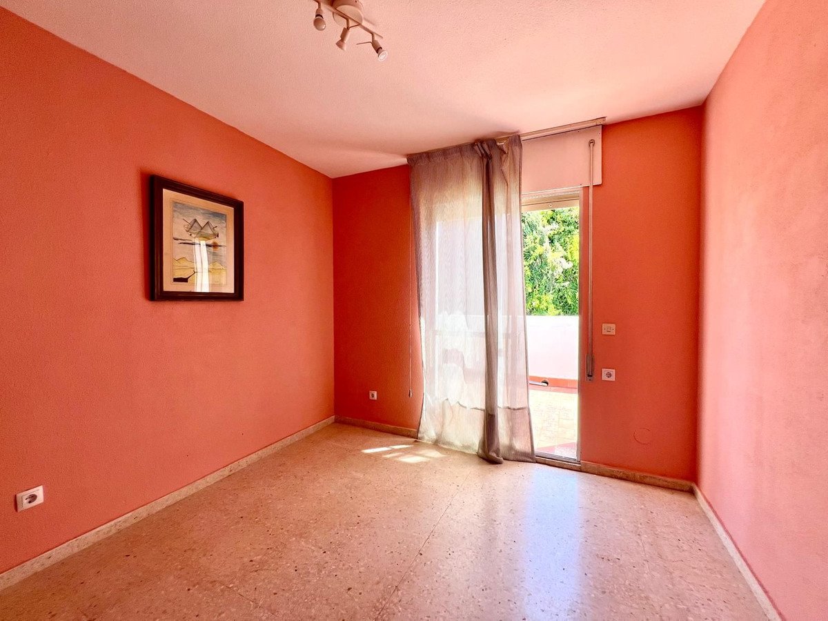 A bright, empty bedroom with coral walls, terrazzo flooring, and access to a sunny terrace with green trees visible outside.