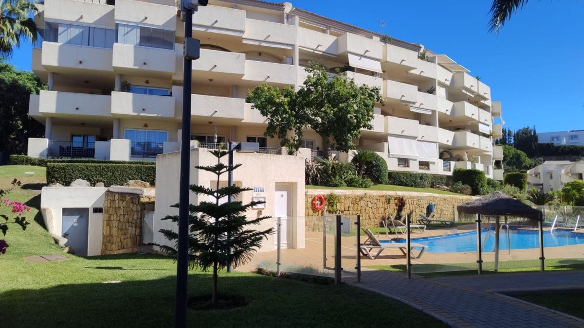 Apartment building with multiple balconies overlooking a pool area with lounge chairs and a thatched umbrella.