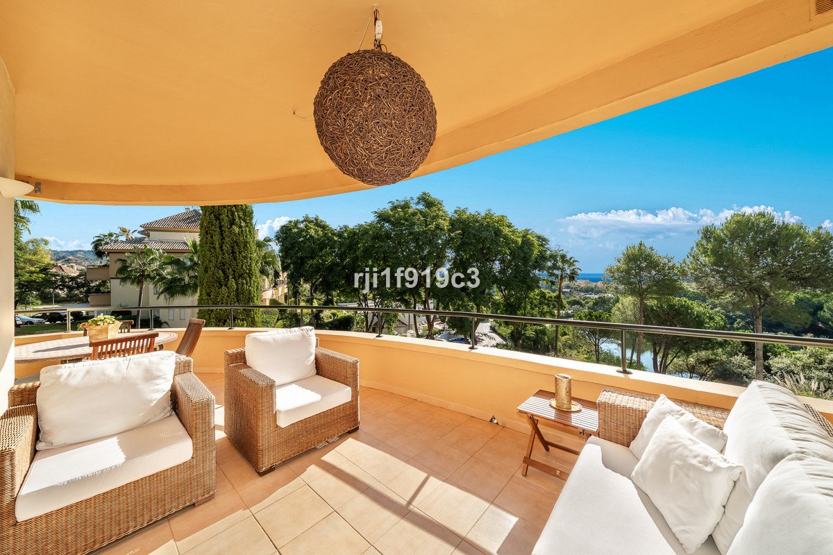 Covered patio with wicker furniture overlooking trees and distant sea view