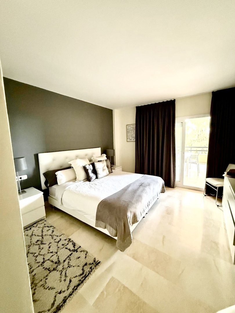 Spacious bedroom with a king-size bed, dark curtains, and access to a balcony with outdoor seating.