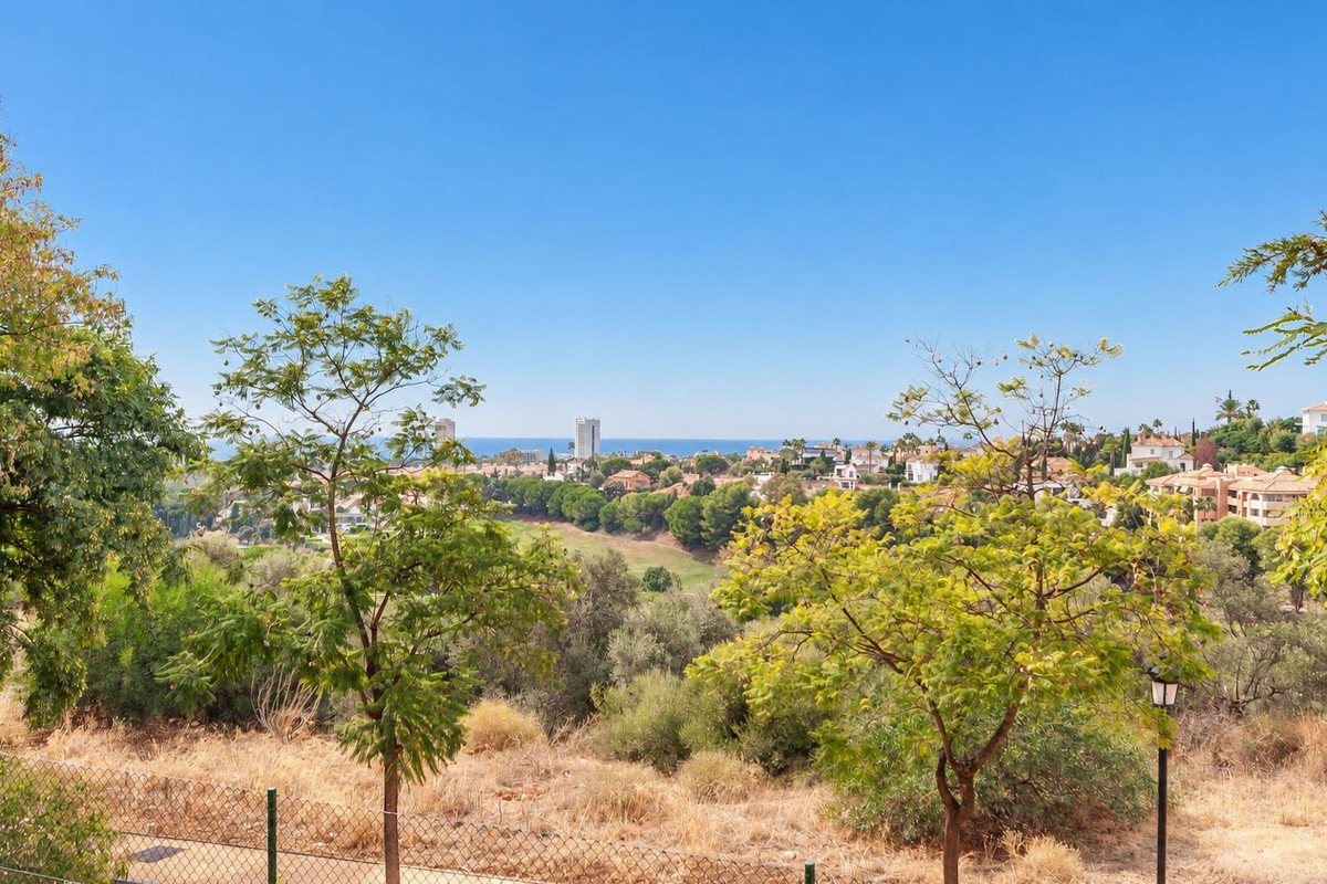 View of a residential area with a golf course and the sea in the distance, framed by trees.