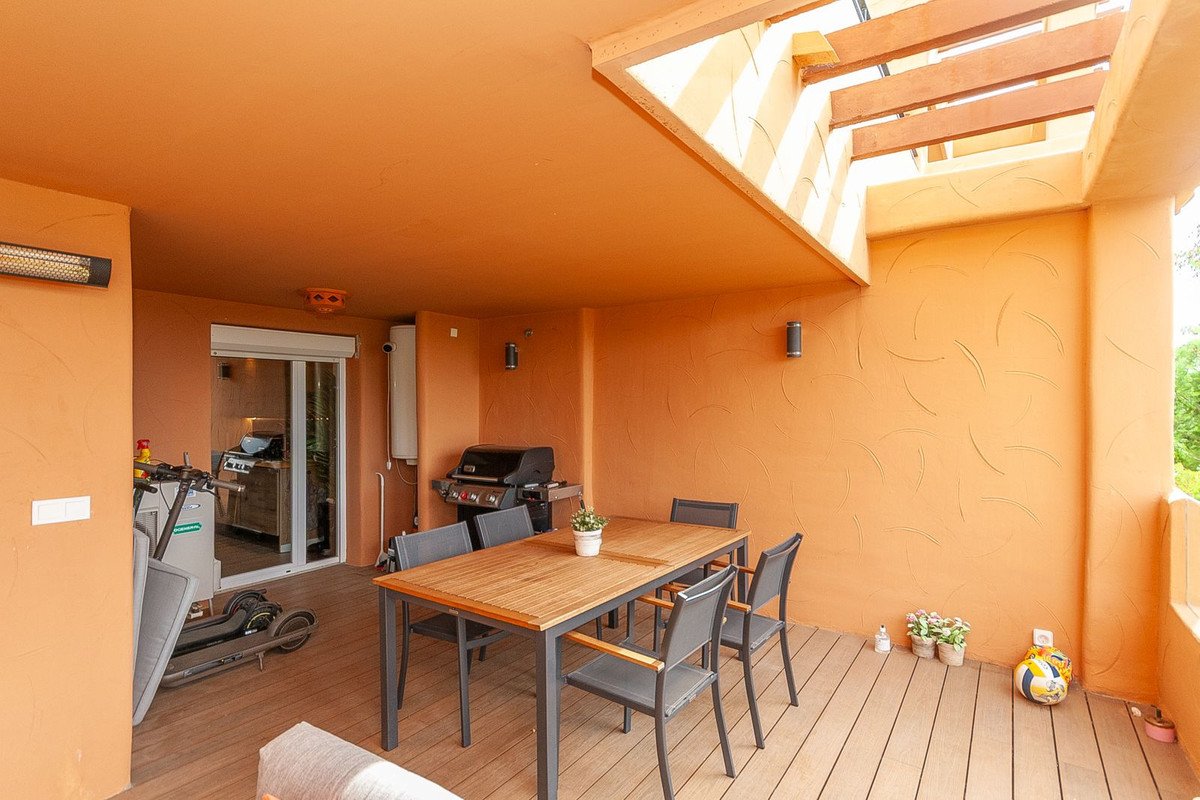 Outdoor terrace with dining table, chairs, grill, and a scooter, scooter. Covered ceiling with wooden beams.
