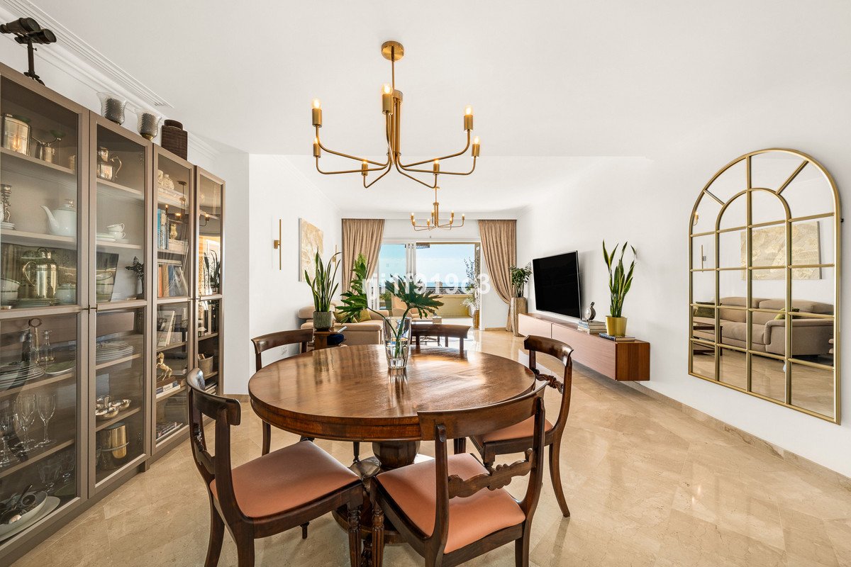 A spacious dining and living area with a round wooden table, display cabinets, and a view of the sea through sliding doors.