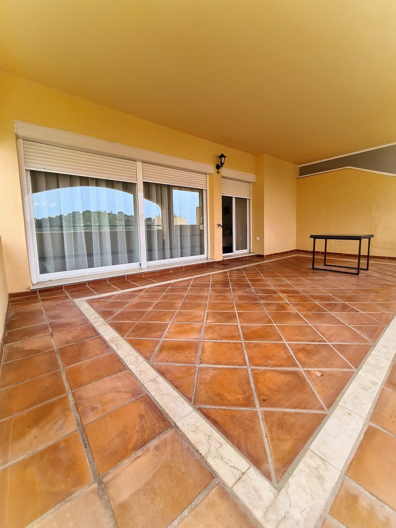 Spacious covered terrace with terracotta tiled flooring, large sliding glass doors, and a small dark table.
