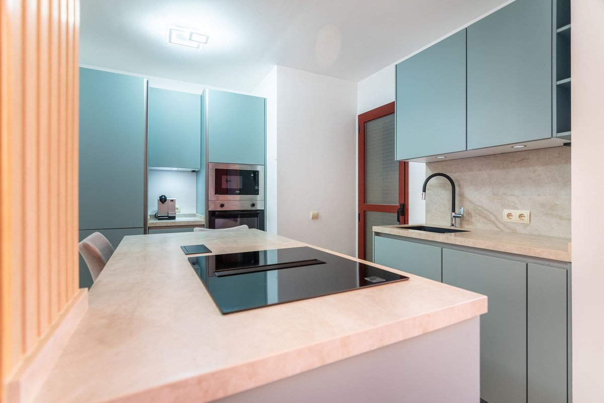 A modern kitchen featuring a light-colored island with an induction hob, light blue cabinets, built-in oven, and microwave.