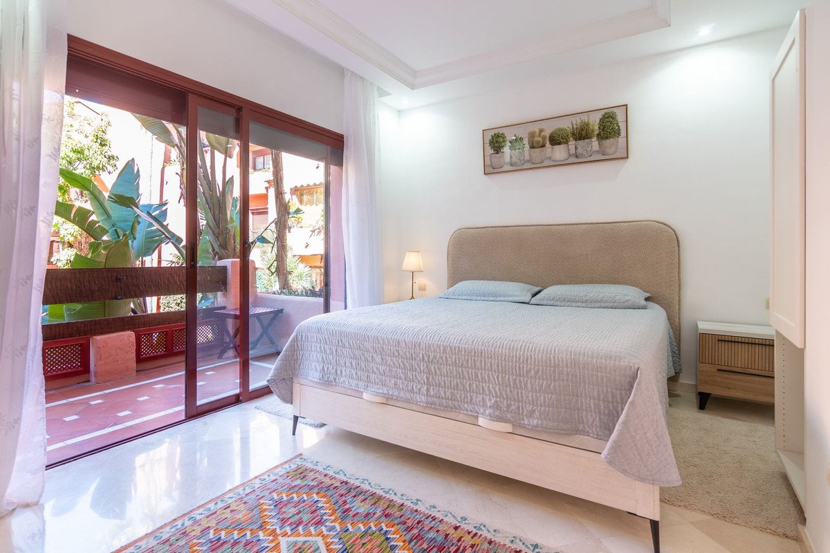 Bedroom with a large bed, light blue bedding, and sliding glass doors opening to a tropical balcony with lush greenery.