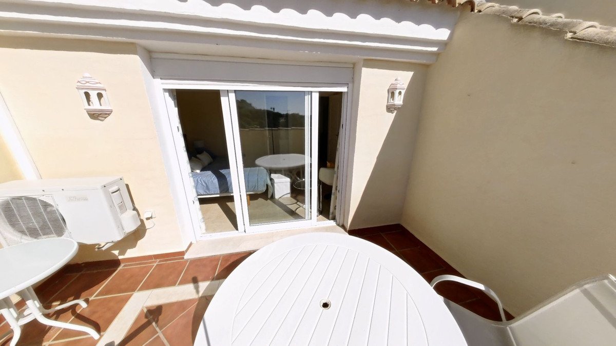 A balcony with outdoor seating and a view into a bedroom with a bed and a table.