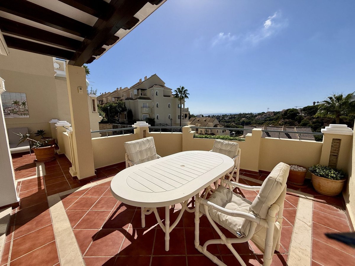 A terrace with a white oval dining table and four chairs, overlooking a scenic view of hills and distant sea.