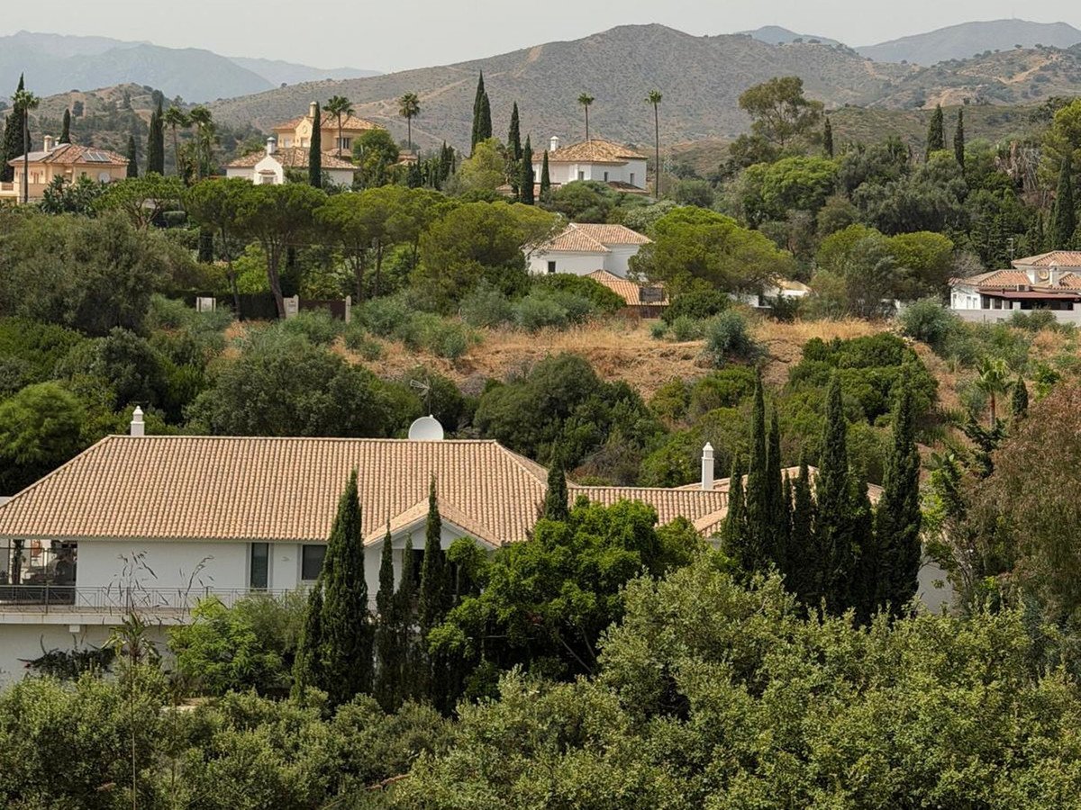 Several villas nestled in a lush, green, hilly landscape with distant mountains under a hazy sky.