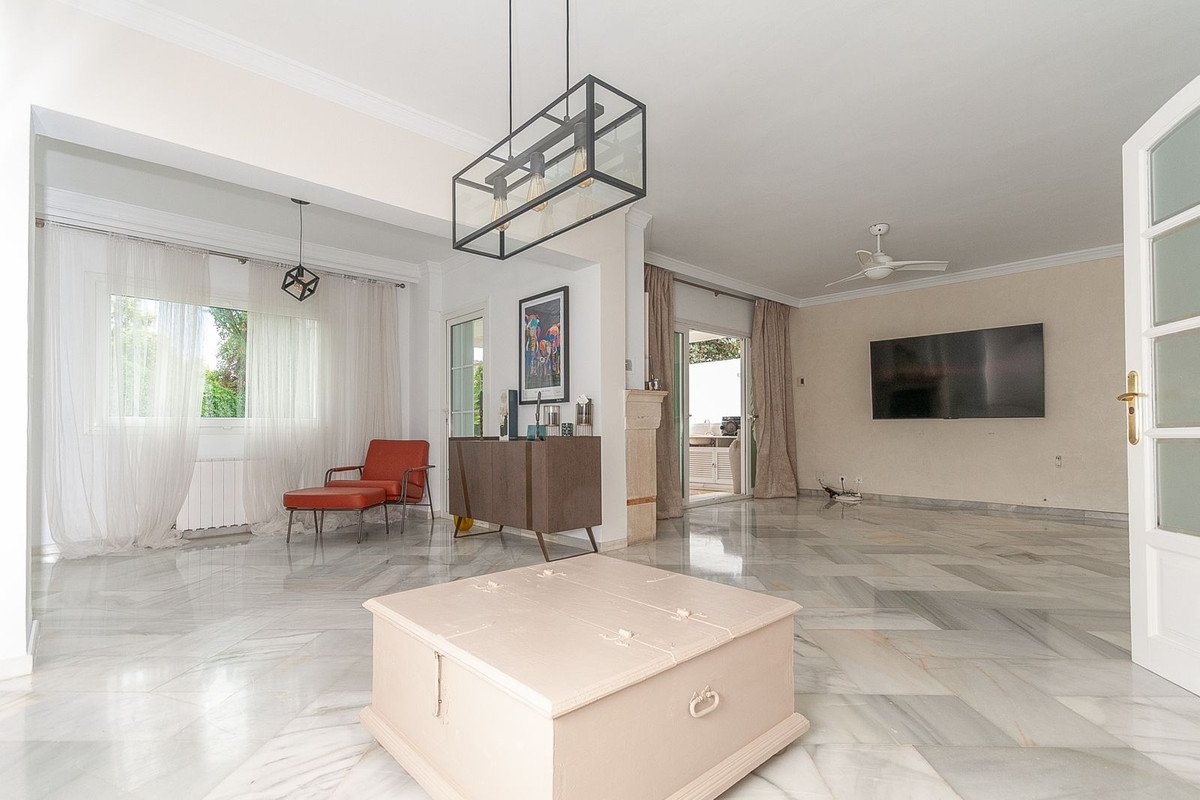 Spacious living room with marble floors, featuring a modern chandelier, orange armchair, and access to a terrace with outdoor seating.