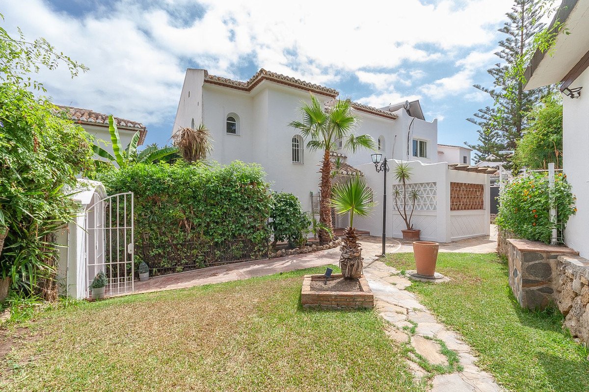 Exterior view of a white villa with a garden, palm trees, and a stone path leading to the entrance.