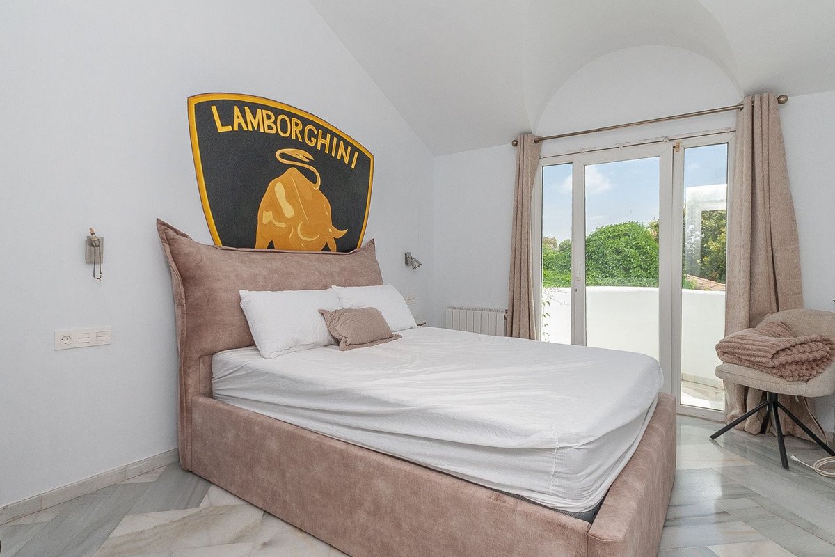 A bedroom featuring a large bed, a Lamborghini logo on the wall, and a door leading to a balcony with green views.
