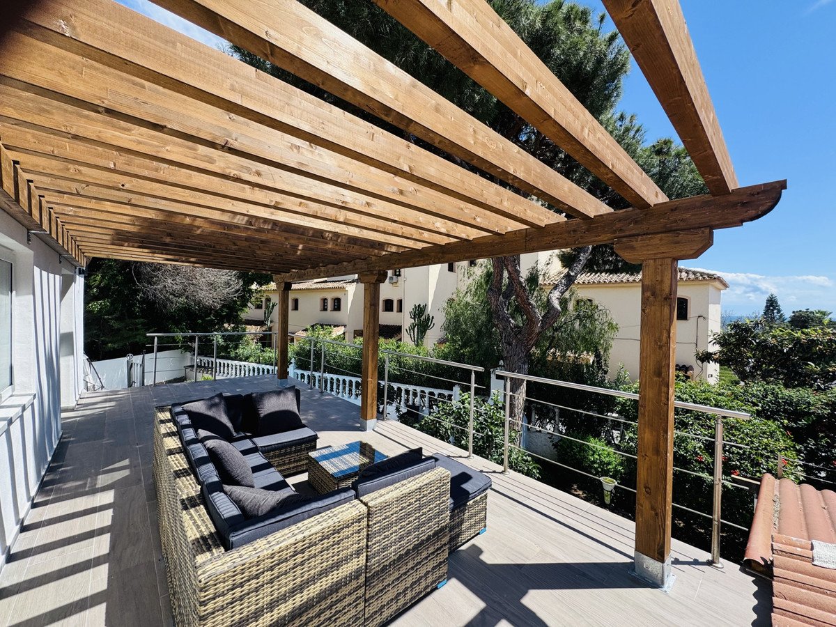 Covered terrace with modern outdoor seating area and a view of surrounding greenery and buildings.