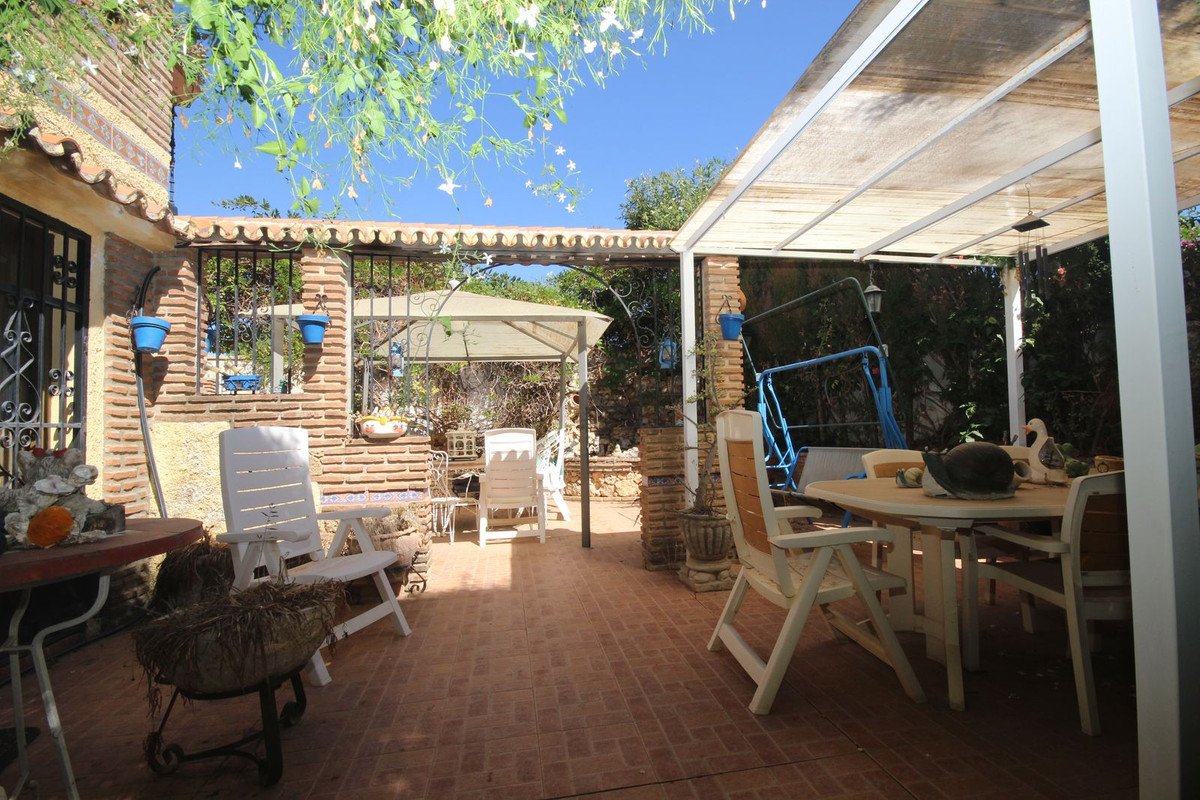 A sunny outdoor patio with white chairs, a table, and a blue swing set under a covered pergola.