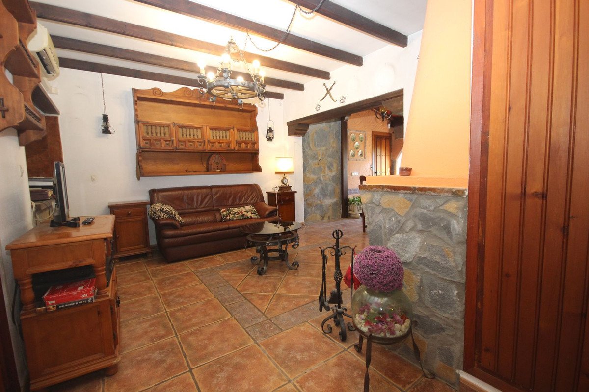 Cozy living room with a brown leather sofa, wooden beams on the ceiling, and decorative shelving.