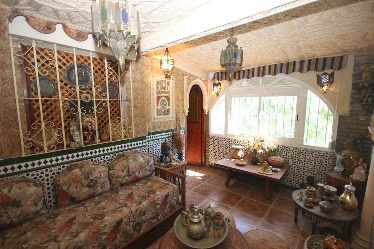 Ornate Moroccan living room with patterned sofa, decorative tiles, traditional lanterns, and a large arched window with garden view.