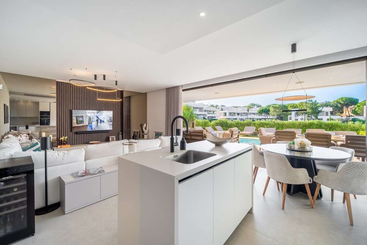 Modern open-plan living area with kitchen island, sofa, and dining table, opening to a pool and garden area.