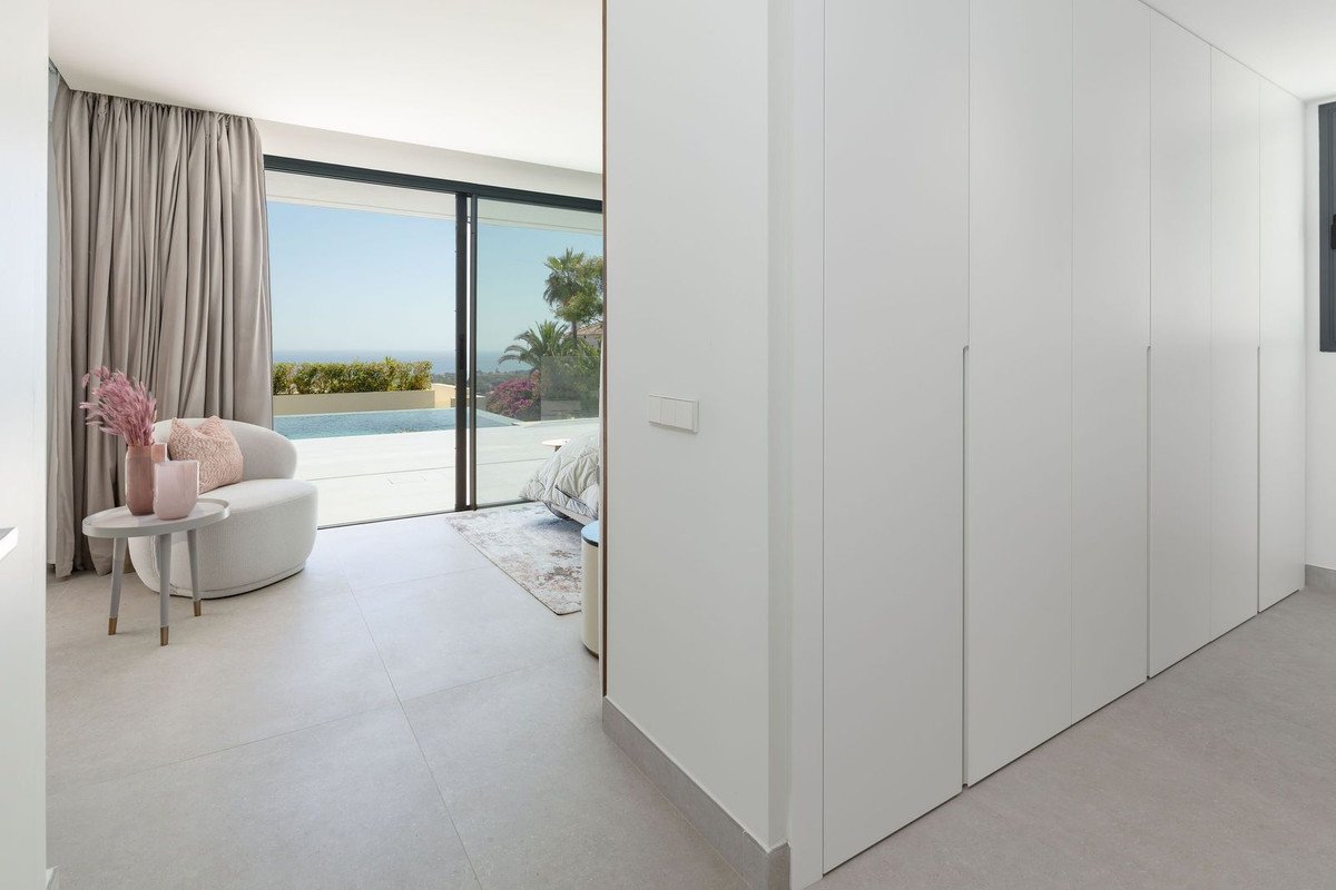 Modern bedroom with floor-to-ceiling windows offering a pool and sea view, complete with built-in wardrobes.
