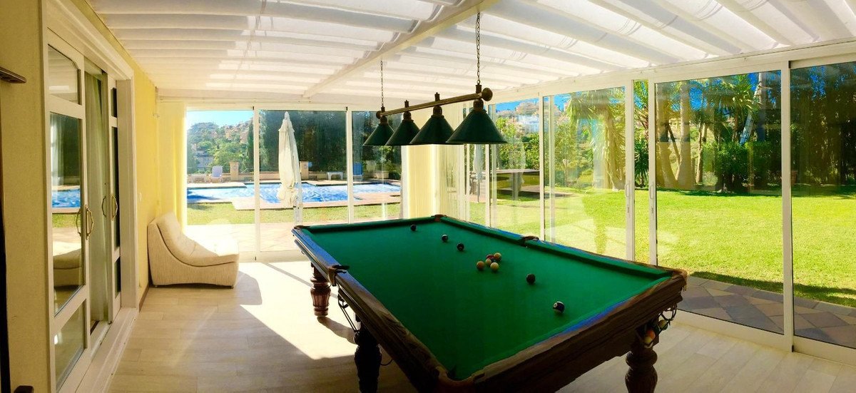Sunroom with pool table and views of a swimming pool and garden. Features a comfortable chair.
