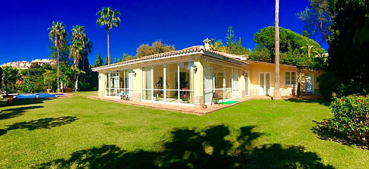 A charming villa with a swimming pool and lush garden, surrounded by palm trees under a clear blue sky.