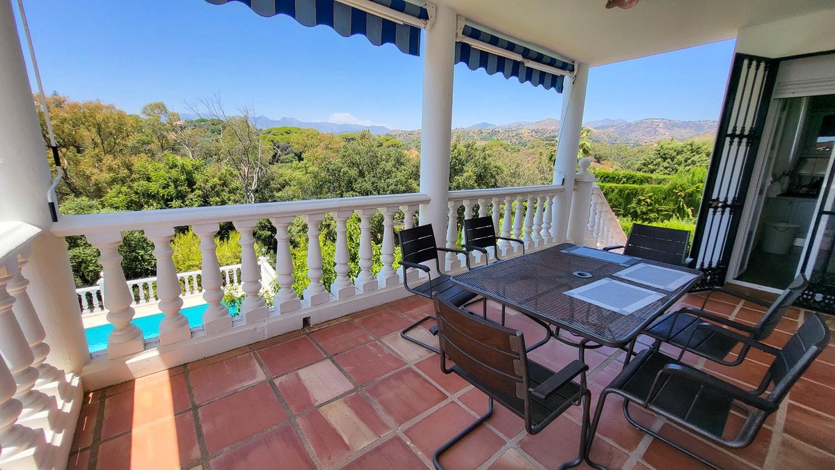 Terrace with dining set, overlooking a pool and lush green landscape with distant mountains under a clear blue sky.