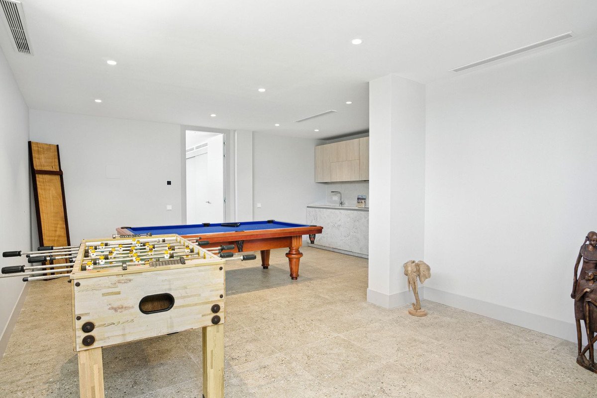 A spacious game room featuring a pool table, foosball table, and a small kitchenette area in the background.