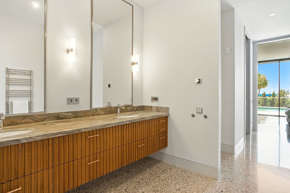 Modern bathroom vanity with dual sinks and a marble countertop, leading to a bedroom with a stunning ocean view.