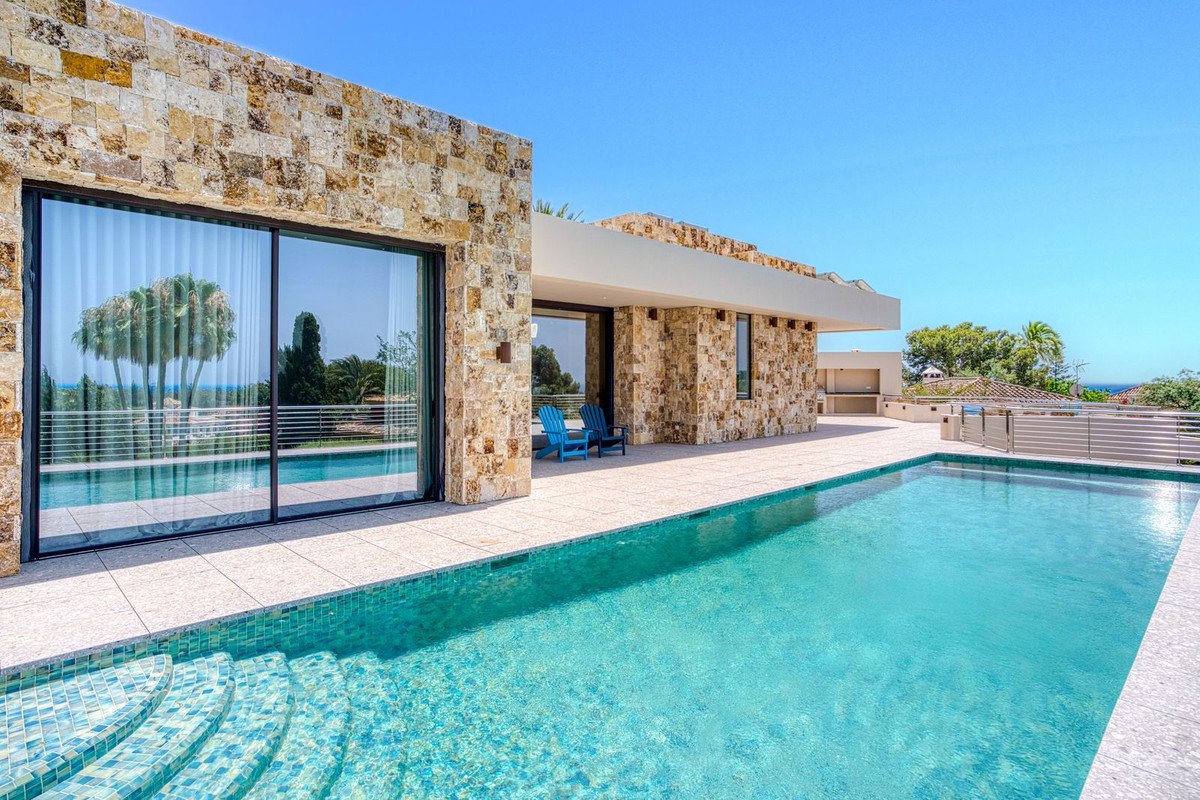 Modern stone villa with a large swimming pool and terrace, offering a beautiful view of palm trees and the sea.