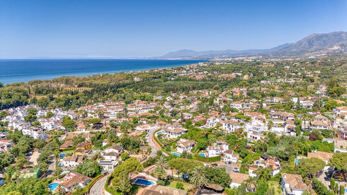 Aerial view of a coastal town with Mediterranean-style houses, lush greenery, and a clear blue sea.