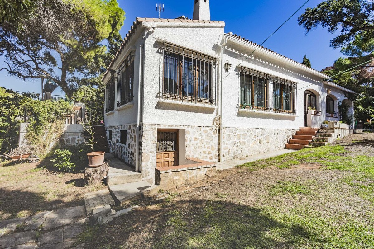 White stone house with garden, trees, and outdoor steps under sunny sky