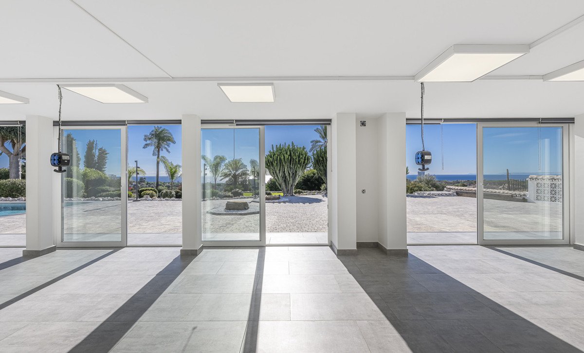 Modern spacious living area with floor-to-ceiling windows offering a panoramic view of the sea and a lush garden.