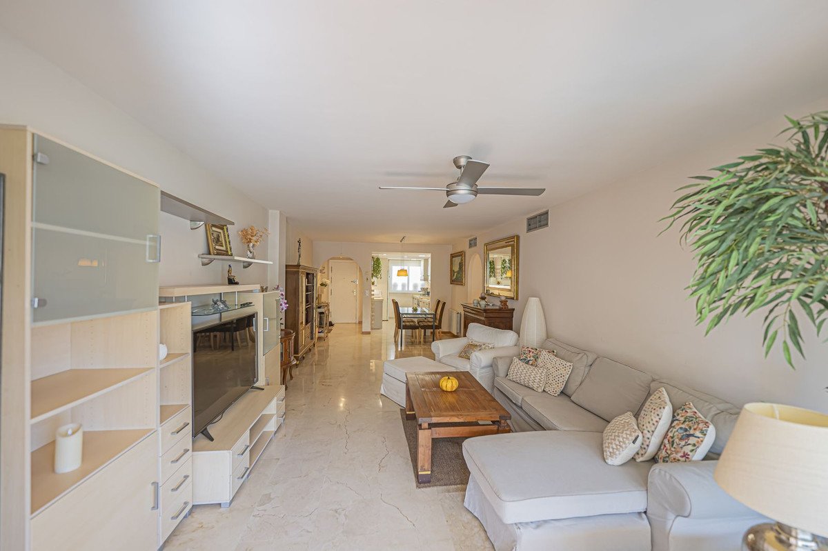 Spacious living room with comfortable sofa, TV unit, and a dining area visible in the background. Features include a ceiling fan and marble flooring.