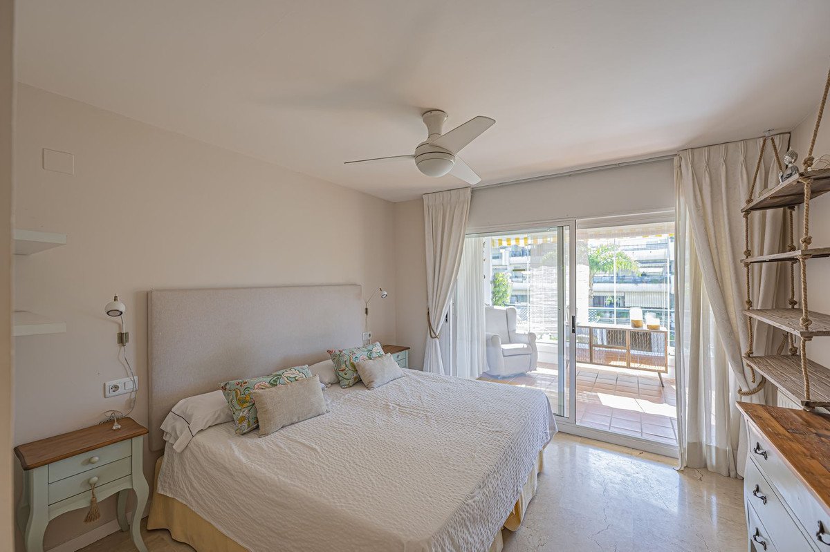 Bedroom with a large bed, ceiling fan, and sliding doors leading to a furnished balcony with a view of buildings.