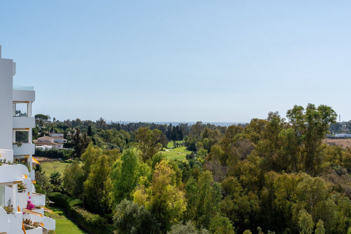 Modern apartment with balcony overlooking lush green golf course and distant sea view under clear blue sky.