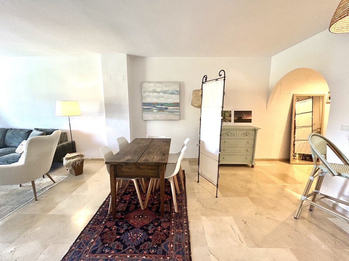 A dining area with a wooden table and chairs, adjacent to a cozy living room with a sofa and armchair.