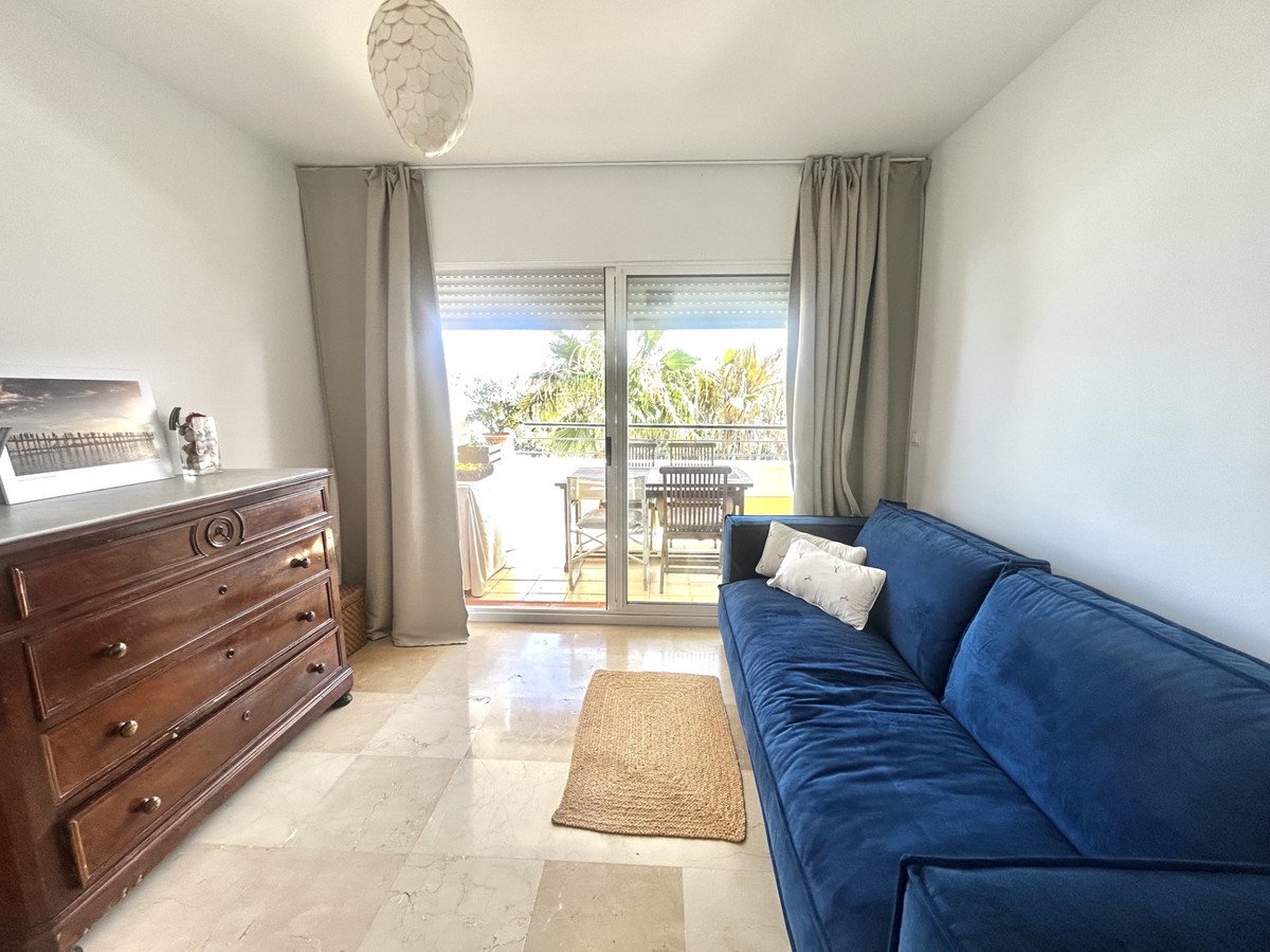 A spacious living room with a large blue sofa, a wooden dresser, and a balcony with outdoor seating, offering a view of trees.