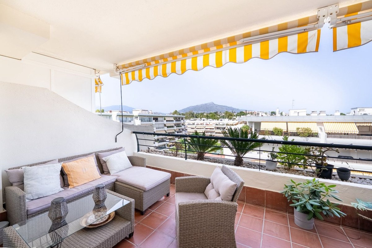 A sunny balcony with wicker seating, striped awning, and mountain view.